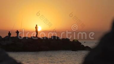 渔夫的剪影，日落时在岩石上钓鱼的人。 120fps